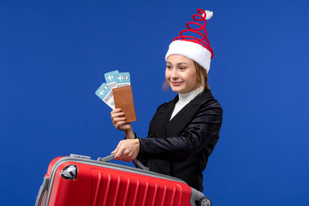职业正面图年轻女性手持包和机票在蓝墙飞机度假前面工作人
