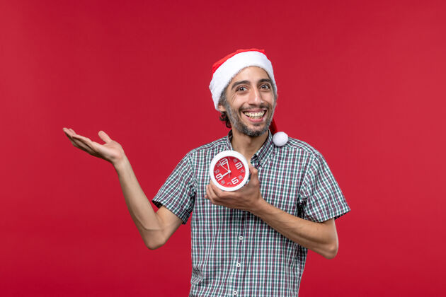 球拍正面图年轻人拿着红墙上带着微笑的时钟红色的情感时间圣诞节时间时钟