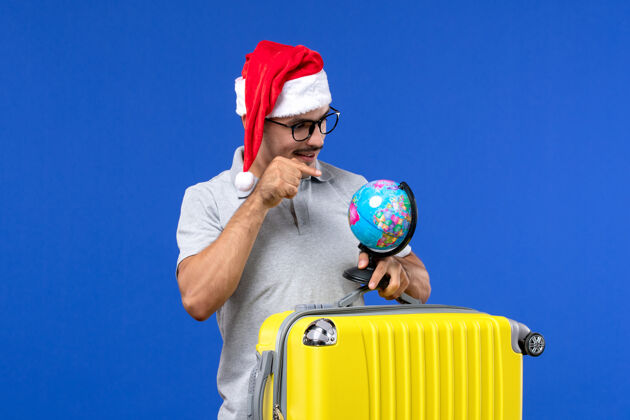 飞机正面图：年轻的男性背着黄色的包和地球仪在蓝色的飞机度假旅行人圣诞节包