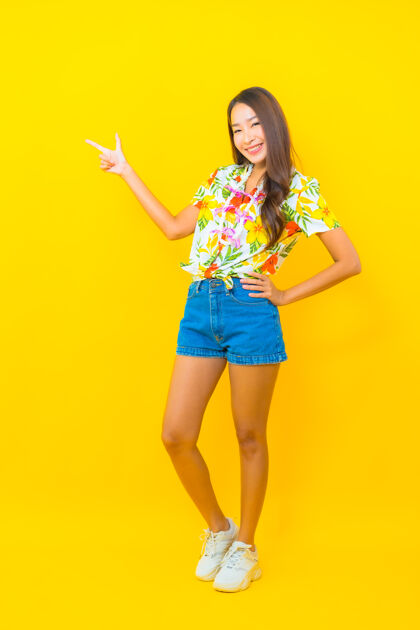 亚洲美丽的亚洲年轻女子身穿五颜六色的衬衫 用手指在黄色墙上拍摄的肖像女人水乐趣
