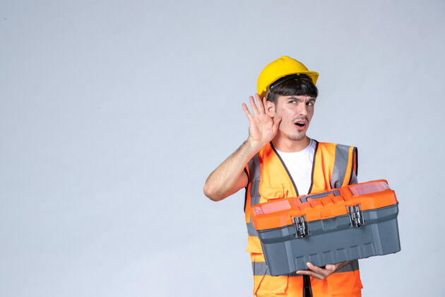 人正面图：年轻的男工人拿着沉重的工具箱 背景是白色的工作承包商工具