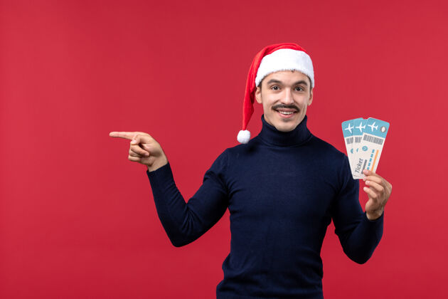 男人正面图：手持红色背景机票的年轻男性圣诞节票年轻的男人