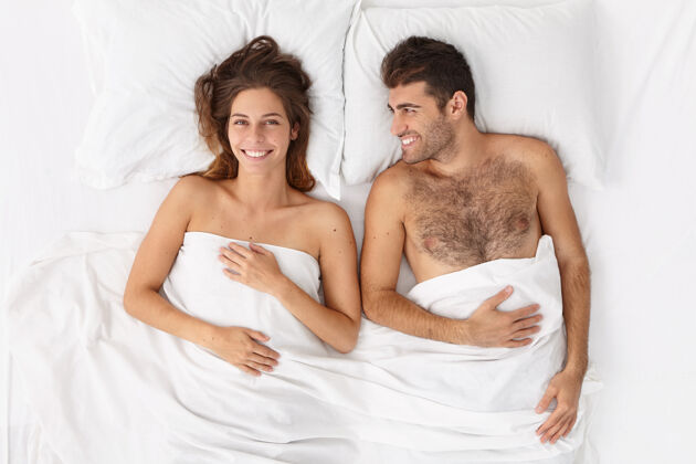 情人甜蜜的新婚夫妇躺在白毯子下的床上 愉快地微笑 一起享受慵懒的一天 感觉休息 健康的睡眠后醒来新婚夫妇有新婚之夜俯瞰图女孩毯子丈夫