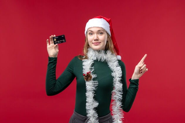 圣诞节正面图：红桌上拿着黑色银行卡的年轻女子人服装视图