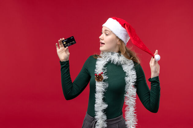 圣诞节正面图年轻女性手持红色背景的黑色银行卡肖像红色黑色