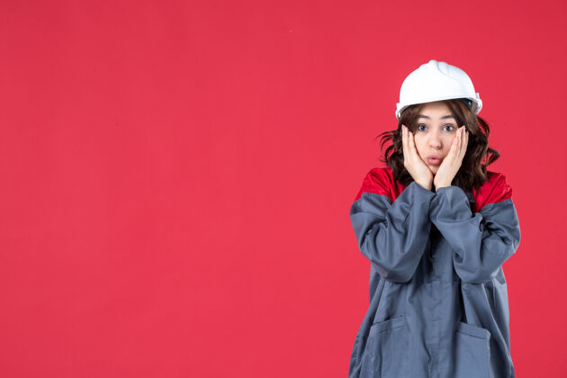 肖像在隔离的红墙上 穿着制服戴着安全帽的惊讶女建筑工人的特写镜头业务建筑师工人