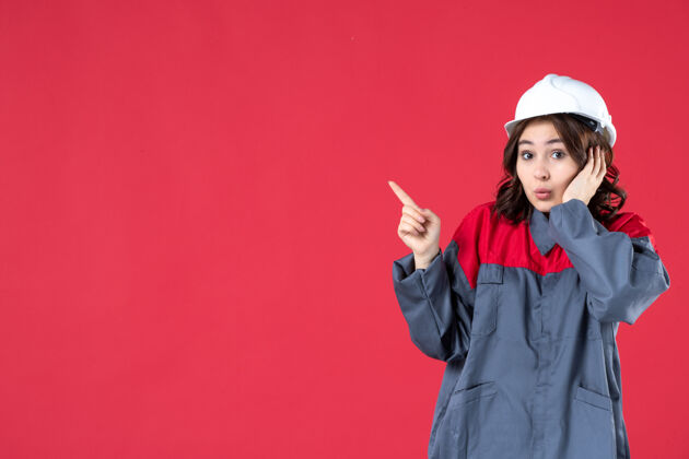 壁板特写镜头中好奇的女建筑工人穿着制服 戴着安全帽 指着隔离的红墙右侧的东西快乐东西吸引力