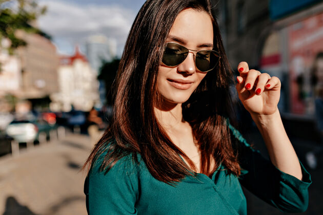 微笑外特写肖像迷人的欧洲妇女戴着黑色太阳镜和绿色衬衫摆姿势朋友积极街头