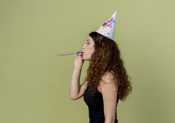 聚会年轻漂亮的女人卷发在节日帽子吹口哨生日聚会的概念侧光帽子节日吹