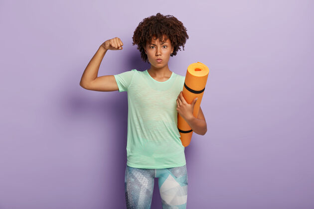 看强壮有力的女人举起手臂 展示肱二头肌 拿着健身垫进行体育训练 穿着运动服运动肌肉瑜伽