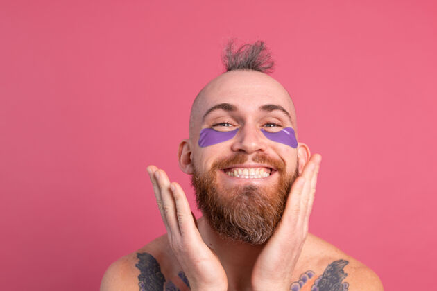卫生欧洲帅哥留着胡子纹身上身的男人戴着紫色眼罩对着镜头摆粉红色的姿势面膜好看男人