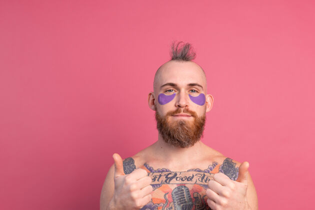 提升欧洲帅哥留着胡子纹身上身的男人戴着紫色眼罩对着镜头摆粉红色的姿势孤独胶原蛋白抗衰老