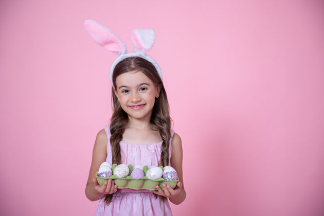 复活节在粉红色的工作室里 一个快乐的小女孩 手上抱着复活节兔子耳朵和一盘鸡蛋兔子摄影棚兔子