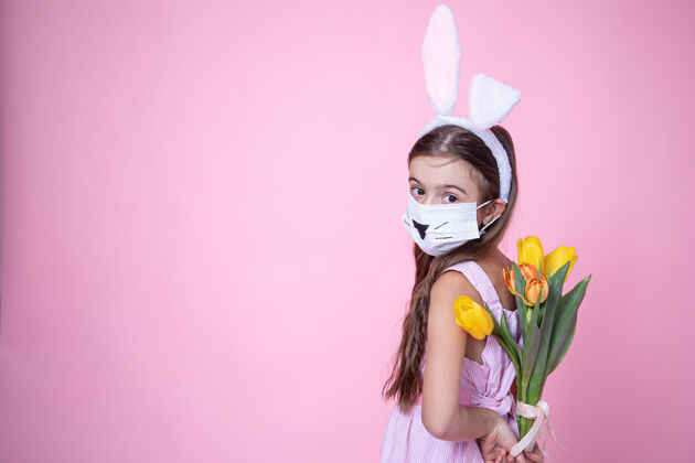 兔子一个戴着医用口罩的复活节兔子耳朵的小女孩手里拿着一束郁金香放在一个粉红色的盒子上检疫花兔子