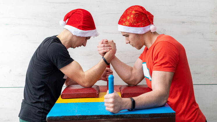 肌肉两个戴着圣诞帽的男人在体育馆摔跤男孩竞争压力