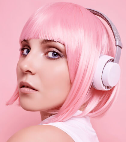 漂亮美丽明亮的潮人女孩的肖像与粉红色的头发享受音乐在耳机上五颜六色女人化妆耳机