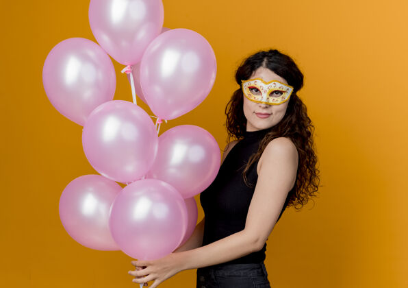年轻年轻漂亮的女人卷发手持一束气球在派对面具快乐快乐的生日派对概念超过橙色美丽面具欢呼
