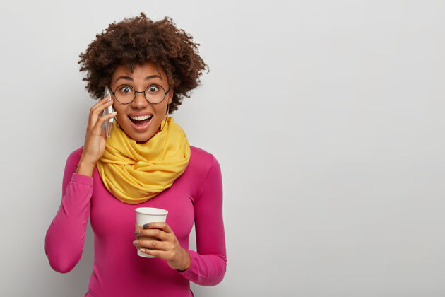 杯子快乐惊喜的非洲裔美国妇女通过智能手机在交谈中得到令人惊叹的消息 喝咖啡休息年轻卷发微笑