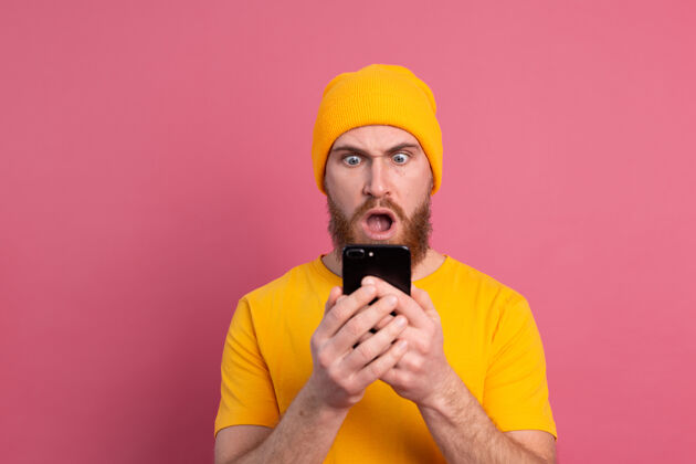震惊照片中的关切震惊了成熟的胡须男性喘息不高兴地拿着智能手机阅读奇怪和令人不安的信息粉红色惊人欧洲惊讶