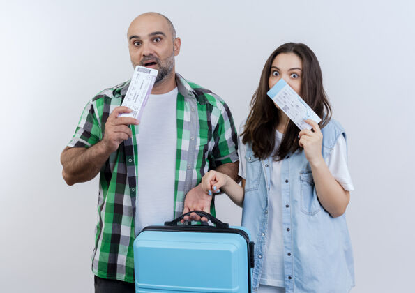 机票给人印象深刻的成人旅行者夫妇拿着手提箱 两人都拿着旅行票摸着下巴看度假两者度假
