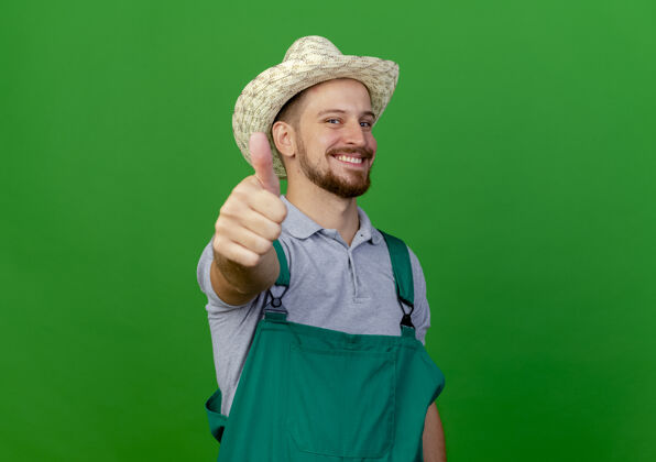向上面带微笑的年轻英俊的斯拉夫园丁 穿着制服 戴着帽子 竖起大拇指帅气花园帽子