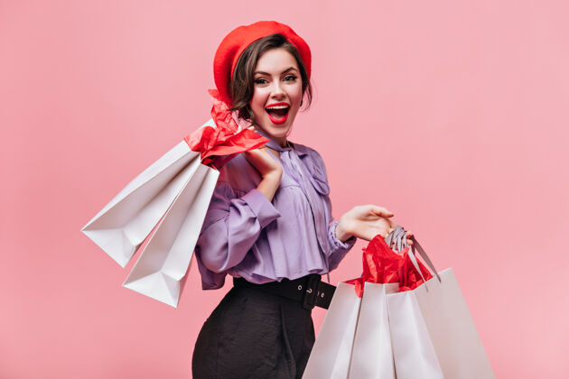 漂亮一个戴着红帽子 黑裤子 浅衬衫的女人在购物后笑着拿着包裹摆姿势脸优雅女士