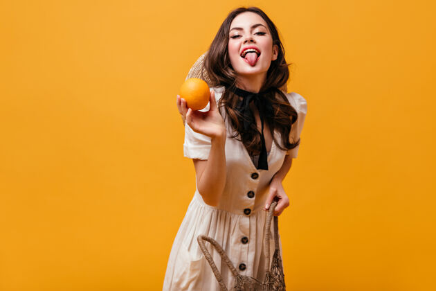 女孩快乐的黑发女孩拿着购物袋 橙色和显示她的舌头孤立的背景橙色背景肖像女士