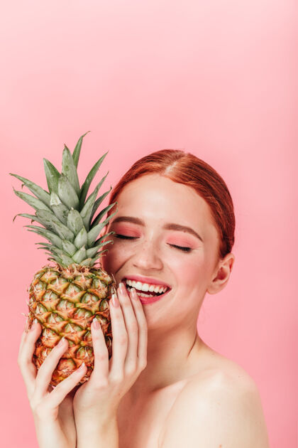 孤立于粉色灵感来自手持菠萝的女模特粉色背景下 带水果的笑姜女孩的摄影棚照片快乐新鲜表情