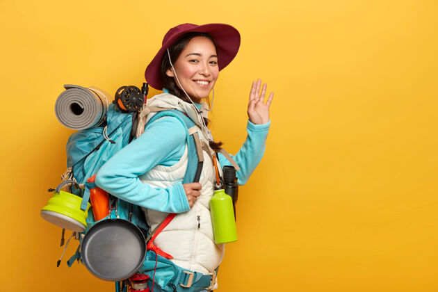背包满脸笑容的亚洲女人背包有着欢快的表情 对着镜头挥舞着手掌 把所有必要的东西都装在大背包里游客室内包
