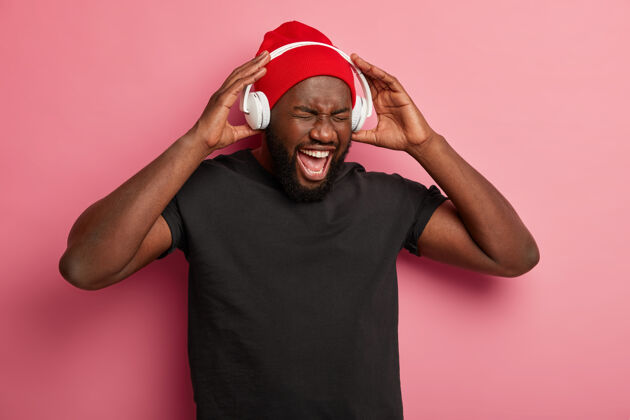 媒体非裔美国人喜欢音乐播放器或录音机 手戴耳机 一边听流行歌曲一边玩得很开心 被隔离在粉红色的墙上聆听积极旋律