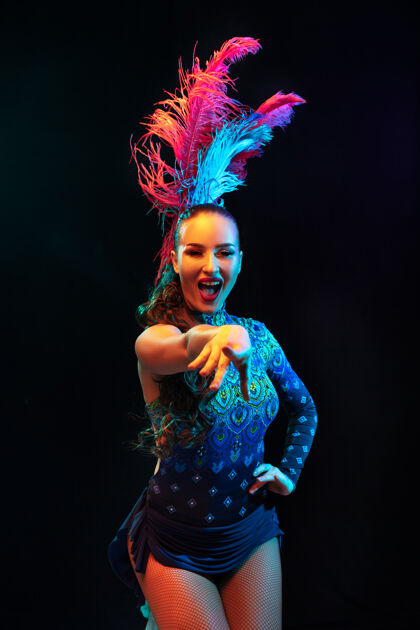 河指向嘉年华美丽的年轻女子 霓虹灯下黑色墙上羽毛的时尚化装服装广告空间节日庆典 舞蹈 时尚节日时间 派对羽毛巴西威尼斯人