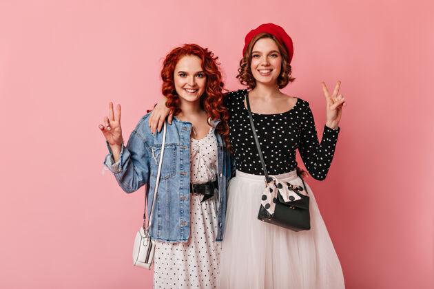 年轻人两个朋友在粉红色背景下拥抱的正面照片微笑女孩展示和平标志的摄影棚照片生姜孤立的粉色粉色背景