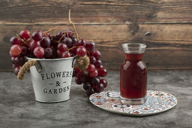 果汁大理石桌上放着一桶红色的新鲜葡萄和一杯果汁玻璃红色新鲜