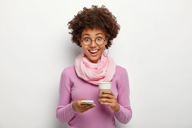 饮料好笑好看的卷发女人用手机喝外卖咖啡 心情愉快 浏览社交媒体女性应用程序设备
