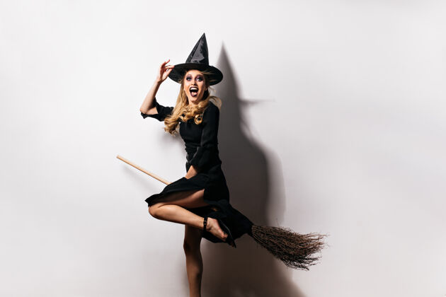 巫术穿着狂欢节服装的感性女孩在万圣节表达快乐迷人的金发女郎戴着魔法帽女巫扫帚成人