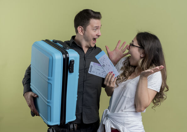 夫妇一对幸福的年轻游客 一男一女拿着手提箱和机票 站在轻薄的墙上 神情惊讶女人飞机年轻人