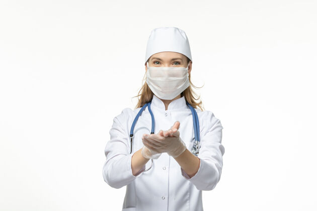 正面正面图：女医生穿着白色医疗服 戴着防护面罩 因冠状病毒在淡白色的墙壁上传播疾病-大流行性疾病视图女性到期