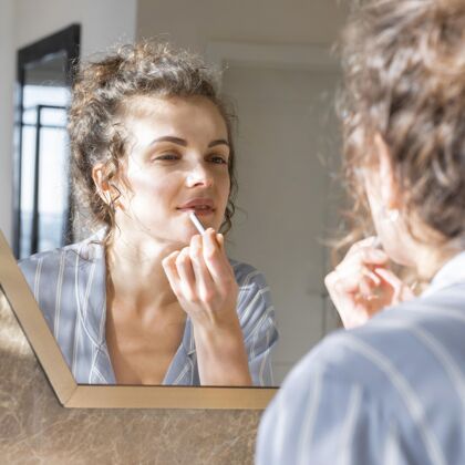 唇膏女人看着镜子 涂上唇膏模特室内Selfcare