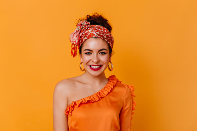 时尚心情很好的年轻女孩在橙色的空间里微笑着穿着橙色上衣 头上戴着围巾的时髦黑发女士看着镜头外表优雅完美