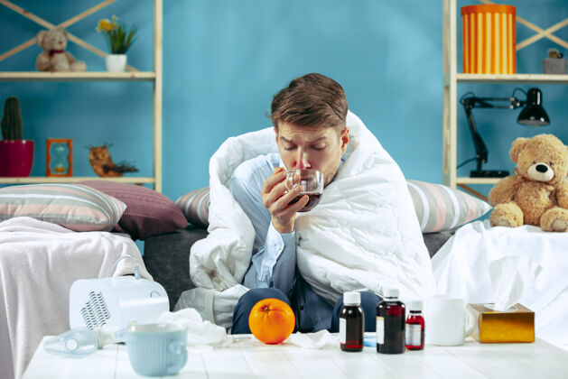 不健康满脸胡须的病人 拿着烟道 坐在家里的沙发上 盖上温暖的毯子 喝着止咳糖浆对疾病 流感 疼痛有概念在家放松感冒疲劳男性
