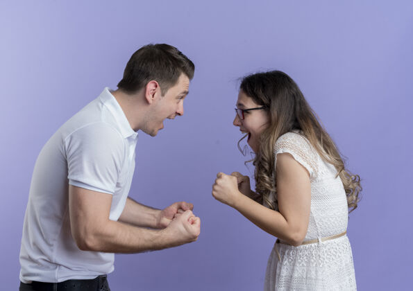 女人一对年轻夫妇站在蓝色的墙壁上互相握拳对视男人夫妇站