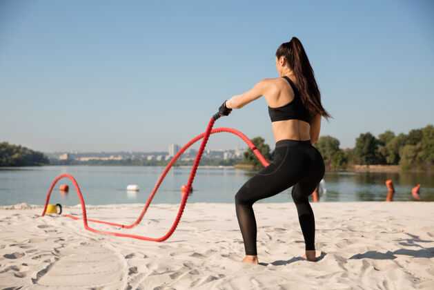 河流年轻健康的女人在沙滩上用绳子锻炼身体交叉力量肌肉