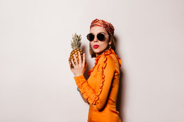 手红唇少女捧着菠萝 白色空间里是一个淘气的女孩 穿着橙色的衣服 戴着墨镜女士情绪衣服