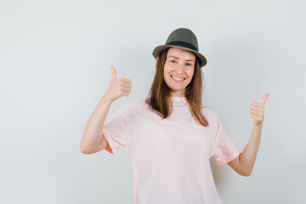 高兴年轻女性穿着粉色t恤 戴着帽子 向上竖起大拇指 看上去很高兴 正前方的景色双人女人成人
