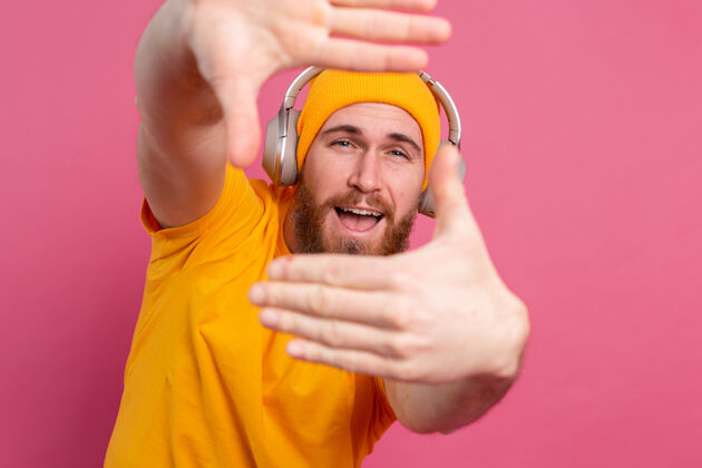 成人帅哥在随意地听着音乐 用耳机隔离在粉色背景上播放列表人物收音机