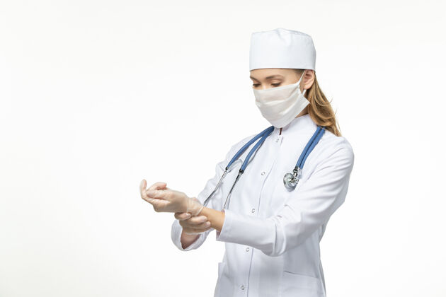 疾病前视图：女医生穿着白色医疗服 戴着无菌口罩 因为冠状病毒在白墙上检查脉搏疾病冠状病毒-大流行性疾病脉搏疾病听诊器