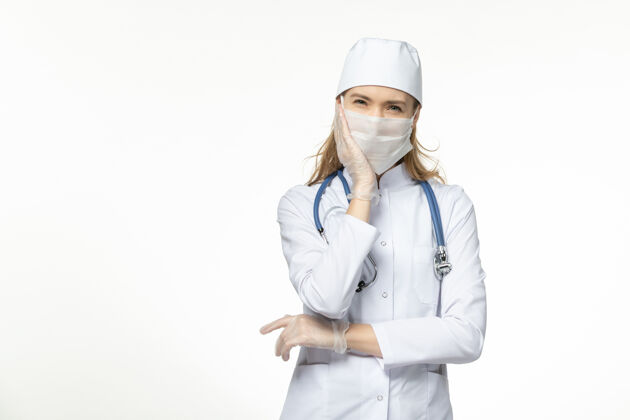 疾病正面图女医生穿着医疗服戴着口罩和手套因冠状病毒重压白墙大流行冠状病毒病疾病病毒大流行