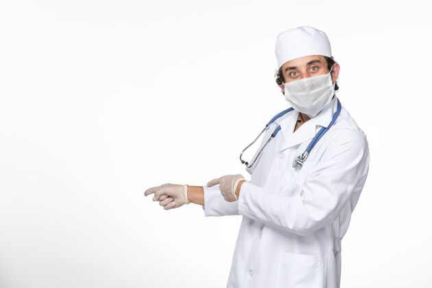 男性正面图男医生穿着医疗服 戴着无菌口罩 以防冠状病毒在白墙上飞溅大流行专业查看