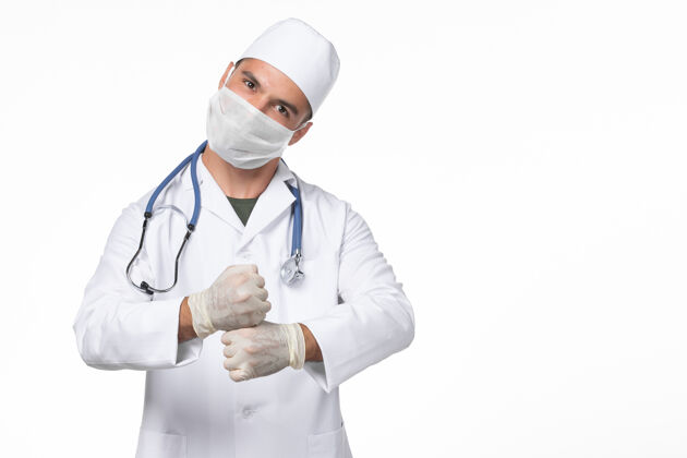 冠状病毒防护正面图：男医生穿着医疗服 戴着口罩 因为白墙上有冠状病毒大流行性病毒病外套视野听诊器
