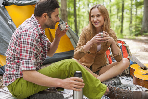 野营一对放松的情侣在森林里享受和喝咖啡运动森林周末